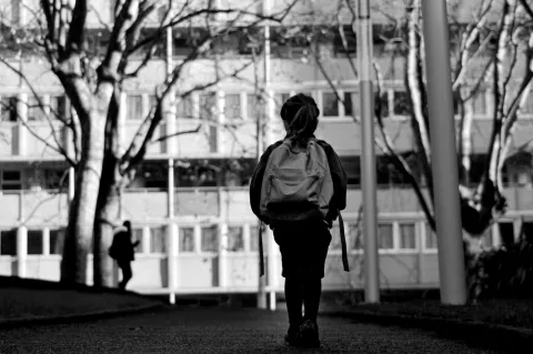 black and white photo of child with backpack facing school building